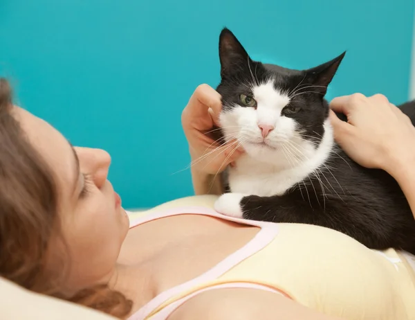 Young woman with a black and white cat in soft focus in the back — Stock Photo, Image