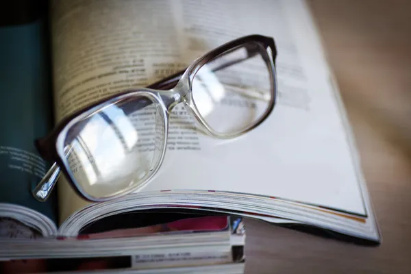 Gafas para leer en una pila de revistas, en enfoque suave — Foto de Stock