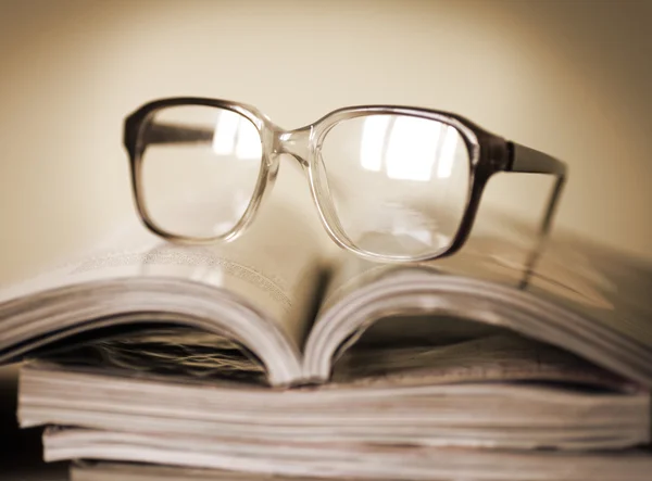 Glazen voor het lezen op een stapel van tijdschriften, in soft focus Sea... — Stockfoto