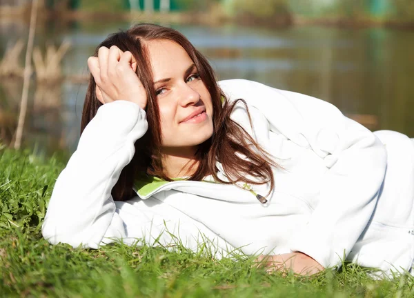 Vrouw in een witte trui liggen op het gras — Stockfoto