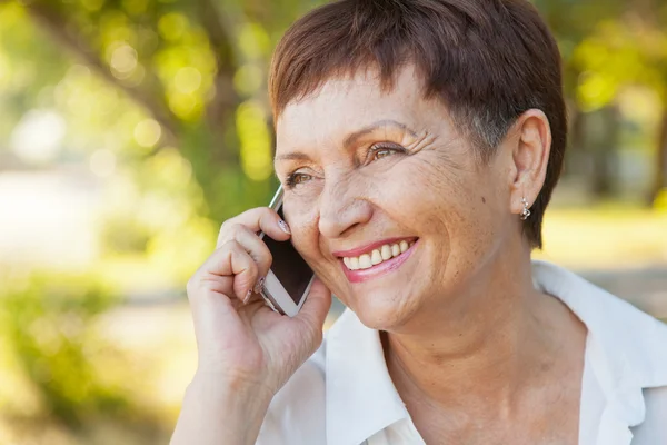 Beautiful woman of 50 years with a mobile phone outdoors — Stock Photo, Image