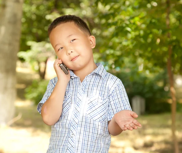 Engraçado asiático menino com um celular em um parque — Fotografia de Stock