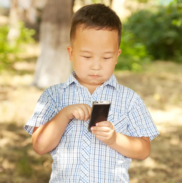 Asyalı çocuk 6 yaşından eski bir parkta bir cep telefonu ile — Stok fotoğraf