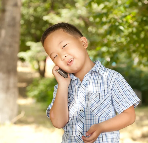 滑稽的亚洲男孩，与在公园里的移动电话 — 图库照片