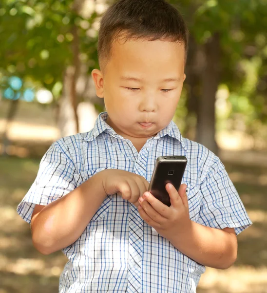 Asijské boy 6 let s mobilním telefonem v parku — Stock fotografie