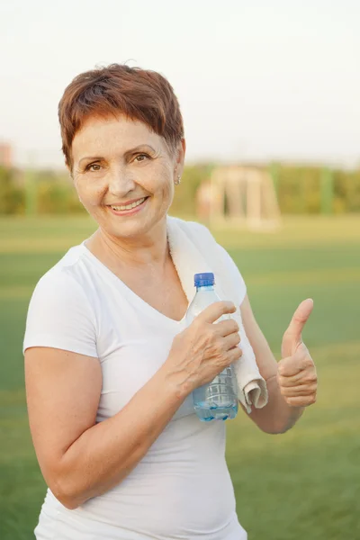 Спортивная женщина 50 лет с бутылкой воды, на открытом воздухе — стоковое фото