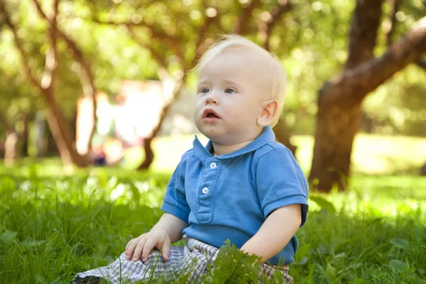 Grappige kleine jongen zittend op het gras in het park — Stockfoto