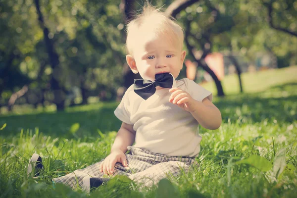 Śmieszne mały chłopiec siedzi na trawie w parku — Zdjęcie stockowe