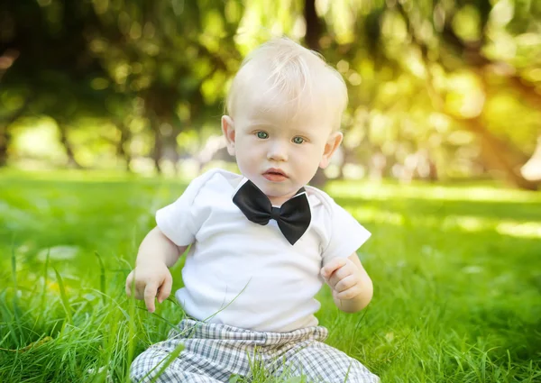 Legrační malý chlapec seděl na trávě v parku — Stock fotografie