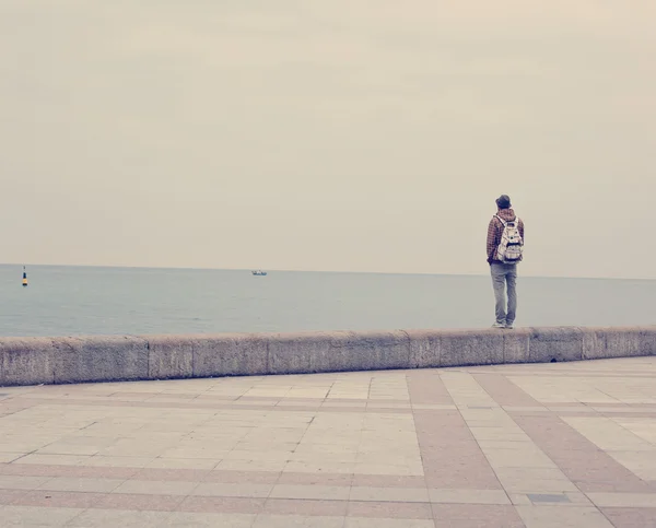 Een jonge man staat op de waterkant en kijken naar de zee — Stockfoto