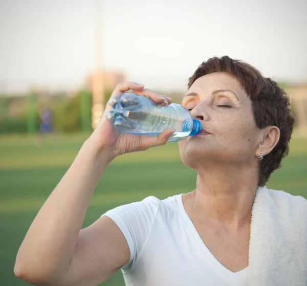 Attraktiv kvinna 50 år gammal, dricka vatten efter fitness — Stockfoto