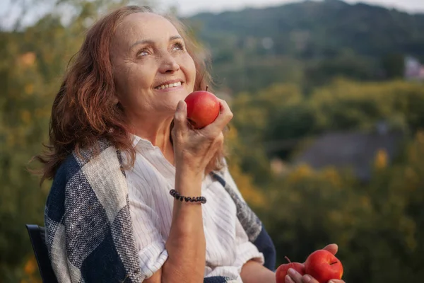 快乐而成熟的老妇人 手里拿着红苹果 坐在自家的庭院里 — 图库照片
