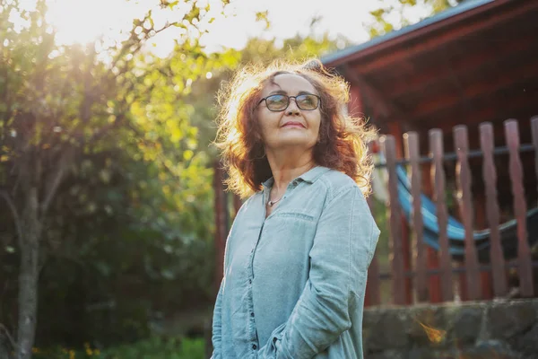 Gözlüklü Güzel Olgun Bir Kadın Batan Güneşin Işınlarında Bahçede Dikiliyor — Stok fotoğraf