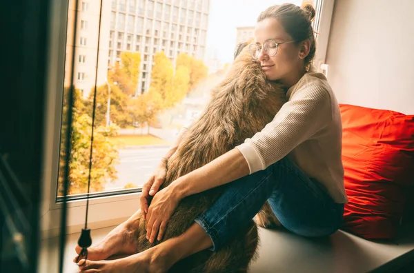 Jonge Vrouw Thuis Knuffelen Haar Hond Aan Het Raam Met — Stockfoto