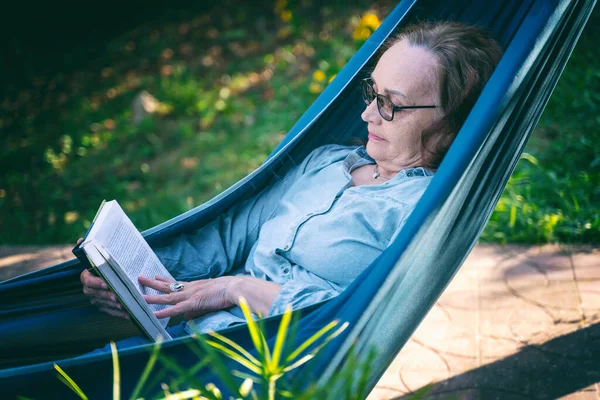 Красивая Зрелая Женщина Очках Читает Книгу Лежа Гамаке Террасе — стоковое фото