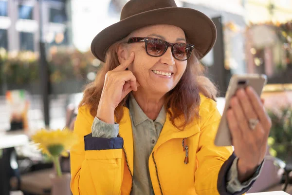Счастливая Зрелая Женщина Шляпе Желтой Куртке Сидит Уличном Кафе Помощью — стоковое фото
