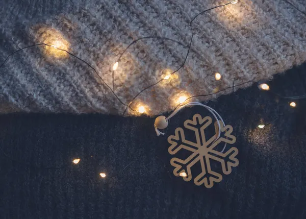 Jouet de sapin de Noël en bois en forme de flocon de neige sur un pull chaud avec guirlande de lumières — Photo