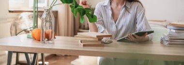 Çekici, mutlu, gülümseyen Avrupalı esmer kadın öğrenci dijital tablet kullanarak evde çalışıyor.