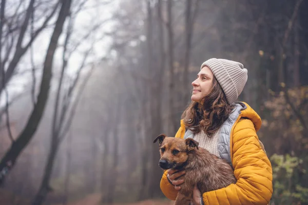 Sarı Ceketli Genç Bir Kadın Köpeği Kollarında Sonbahar Sisli Ormanlarında — Stok fotoğraf