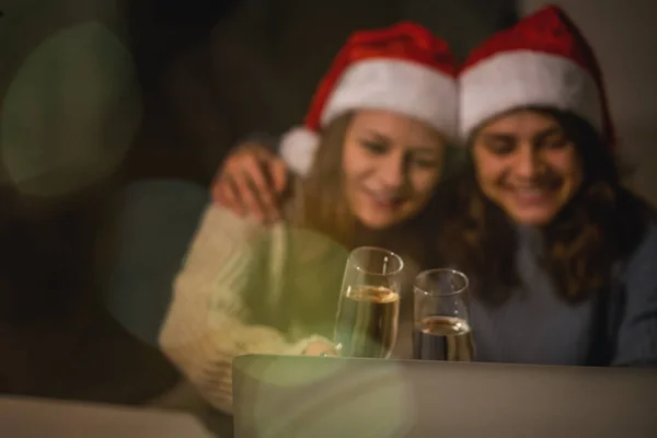 Image floue, fond festif. Deux jeunes femmes heureuses et belles copines couple lesbien avec des verres de champagne en chapeaux de Père Noël rouges célèbrent la nouvelle année et Noël — Photo