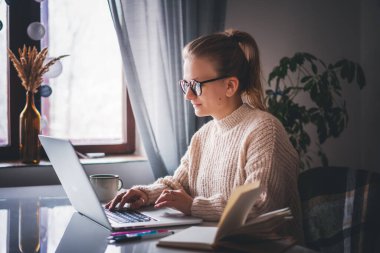 Evde çalışan serbest öğrenci kız bilgisayarını, online işini ve eğitimini kullanarak kahve masasında oturuyor.