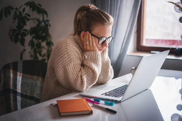 Vážná mladá dívka studentka s brýlemi pozorující pozorně monitor, čtení a poslech přednášky pomocí notebooku, on-line vzdělávání — Stock fotografie