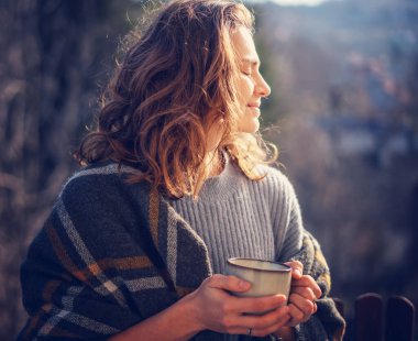 Portrait of relaxed beautiful curly young woman enjoying morning coffee by nature and fresh air on the terrace of a country house