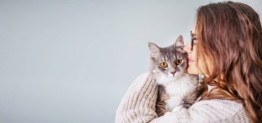 Young cheerful curly girl woman in glasses holding a beautiful gray fluffy cat in her arms
