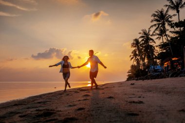 Young happy couple dancing on tropical beach at sunset, honeymoon travel