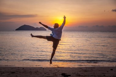 Siluet Genç adam gün batımında tropikal sahilde neşe içinde atlıyor