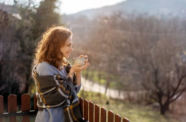 Счастливая жизнерадостная красивая кудрявая молодая женщина наслаждается утренним кофе и видом на горы на террасе загородного дома — стоковое фото
