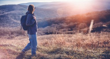Sırt çantalı genç bir kadın dağlarda bahar günü doğa yürüyüşü yapıyor.