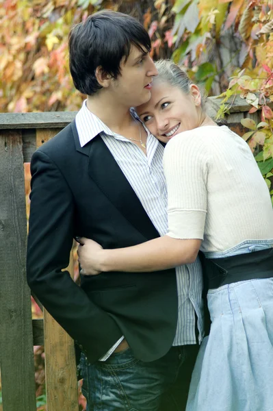 Couple hugging near the fence in the background of autumn leaves — Stock Photo, Image