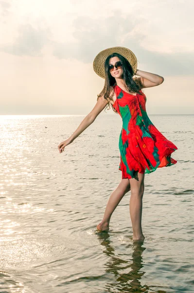 Flicka i en sommarklänning och stråhatt dansa på stranden — Stockfoto