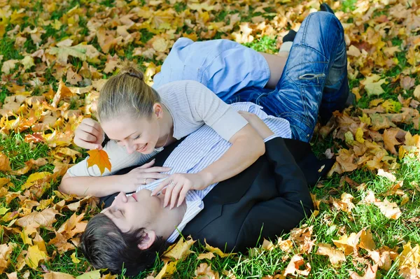 Casal jovem deitado em folhas de outono — Fotografia de Stock