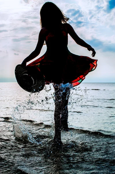 Girl in a summer dress and straw hat splashes of ocean water — Stock Photo, Image