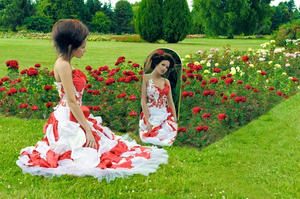 Una hermosa joven en un vestido rojo mira en el espejo —  Fotos de Stock