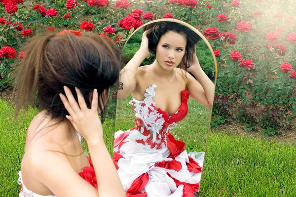 一个美丽的年轻女孩，在一件红衣服看着镜子 — 图库照片