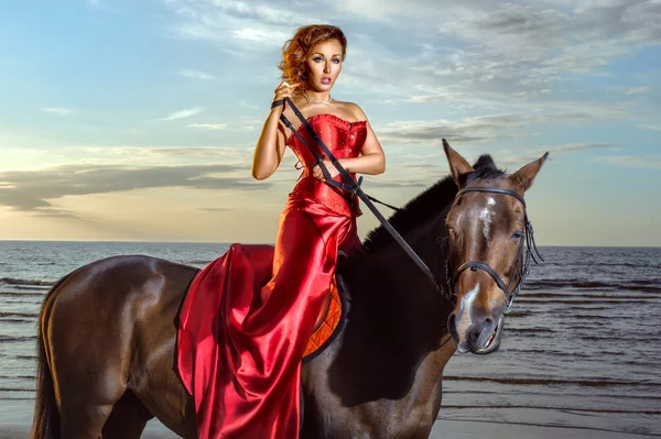 Γυναίκα σε ένα κομψό κόκκινο φόρεμα με ένα άλογο στην παραλία — Φωτογραφία Αρχείου
