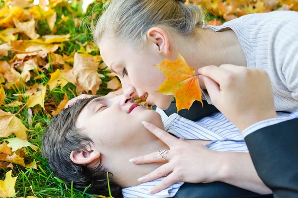 Pareja joven acostada en hojas de otoño y beso —  Fotos de Stock