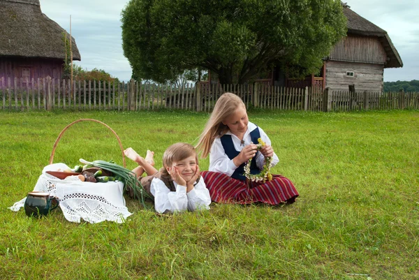 Kleine Jungen und Mädchen sitzen auf einem Rasen in lettischer Nationalkleidung — Stockfoto