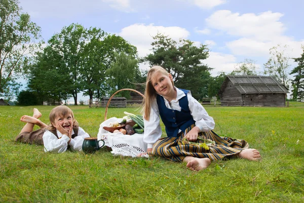 Kleine Jungen und Mädchen sitzen auf einem Rasen in lettischer Nationalkleidung — Stockfoto