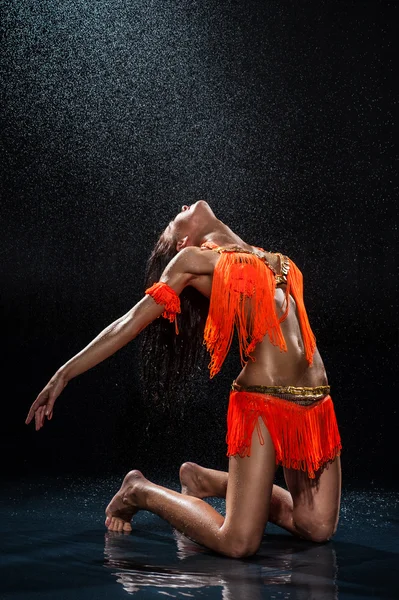 Frau tanzt im orangefarbenen Kleid unter Regen. Studio — Stockfoto