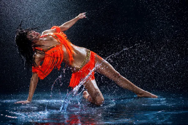 Женщина танцует под дождем в оранжевом платье. Студия — стоковое фото