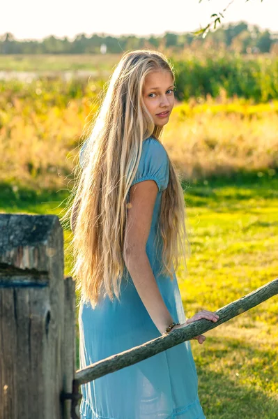 Vacker ung flicka med långa blonda hår i blå klänning på landsbygden — Stockfoto