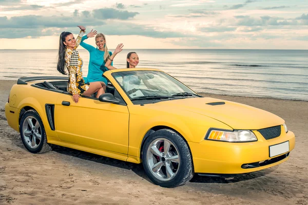 Drie meisjes met sport auto op een strand — Stockfoto