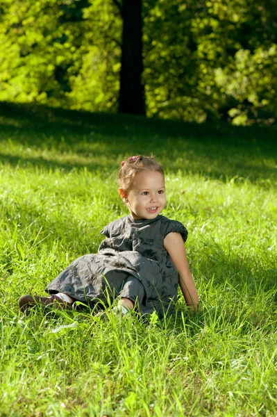 A menina está sentada em um gramado verde na luz do sol da manhã . — Fotografia de Stock