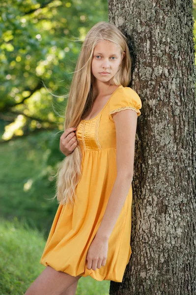 Fille blonde aux cheveux longs en robe jaune appuyé sur l'arbre — Photo