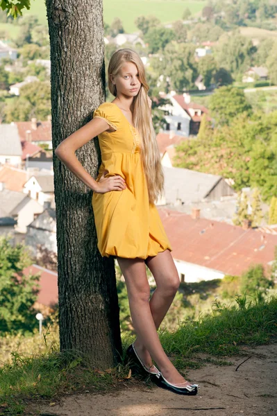 Fille blonde aux cheveux longs en robe jaune appuyé sur l'arbre — Photo