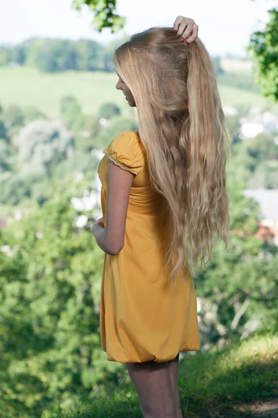 Blond Girl with long hair in yellow dress against rural landscape background — Stock Photo, Image